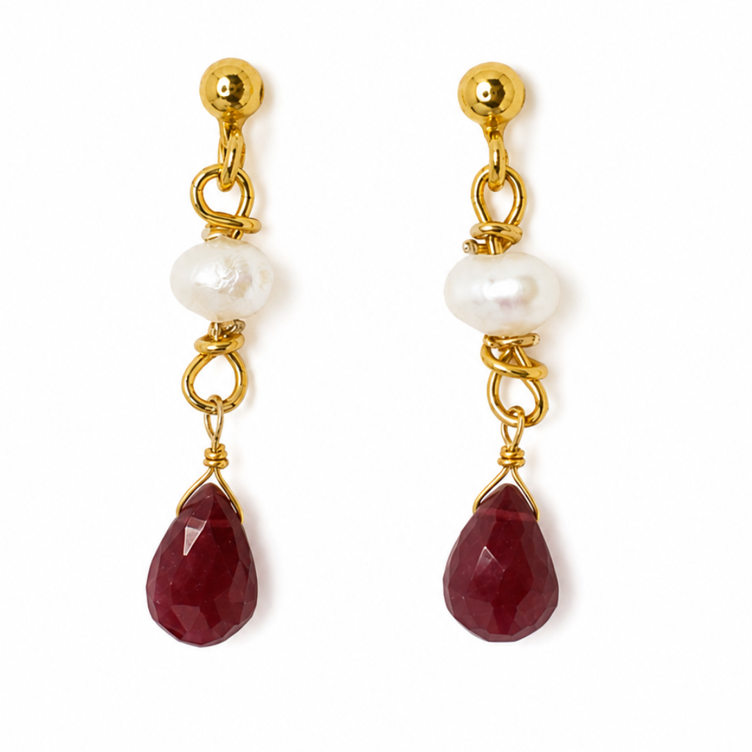 A pair of gold drop earrings featuring a faceted dark red carnelian stone, a white baroque pearl, and a small gold bead on a white background.