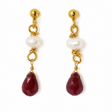 A pair of gold drop earrings featuring a faceted dark red carnelian stone, a white baroque pearl, and a small gold bead on a white background.
