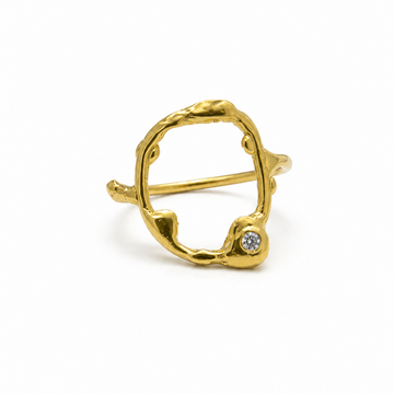 A gold-plated ring with a small round clear gemstone set on one of the lower tips, photographed on a clean white background.