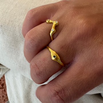 Gold ring with a unique design worn on a finger against a neutral background