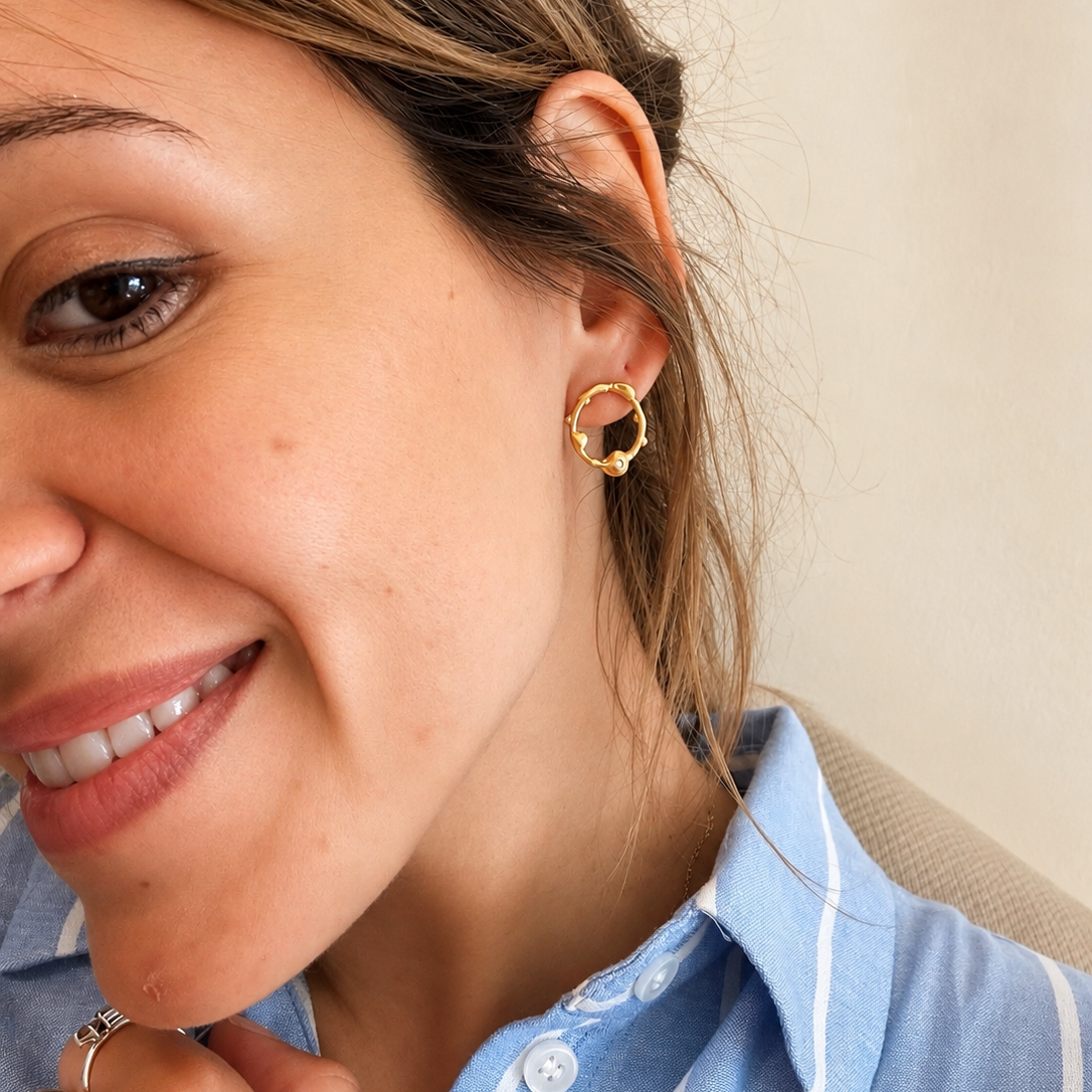Close-up of a woman wearing a gold hoop earring with a neutral background