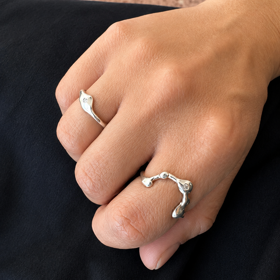 Hand wearing two silver rings on a dark fabric background