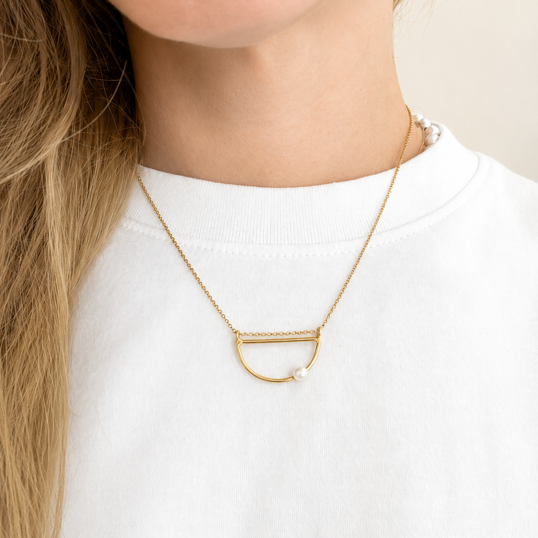 A close-up of a model wearing a delicate gold necklace with a small white pearl accent, styled with a white crewneck top.