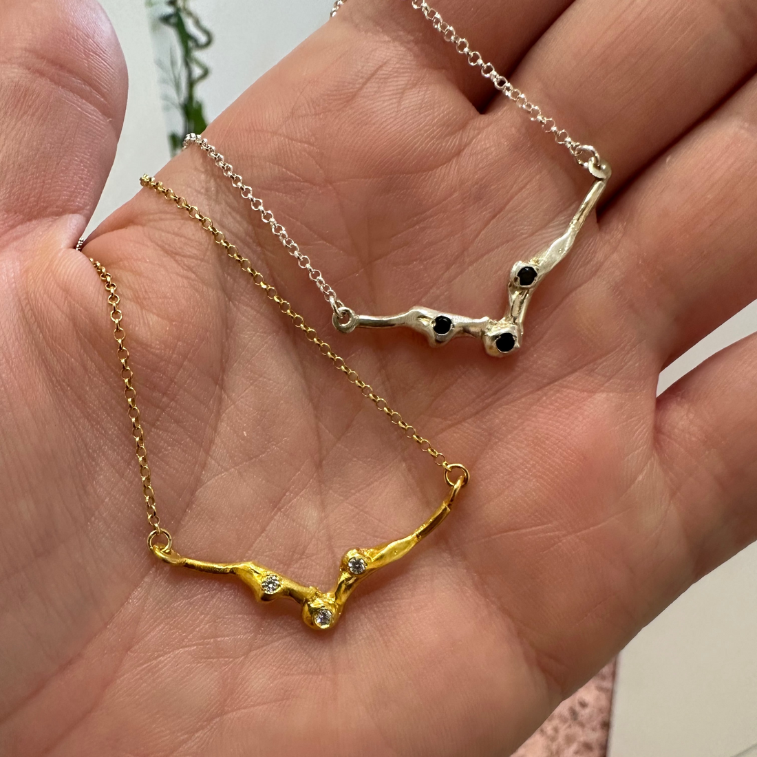 A delicate gold chain necklace featuring a branch-like pendant with small clear gemstones, displayed against a solid white background.