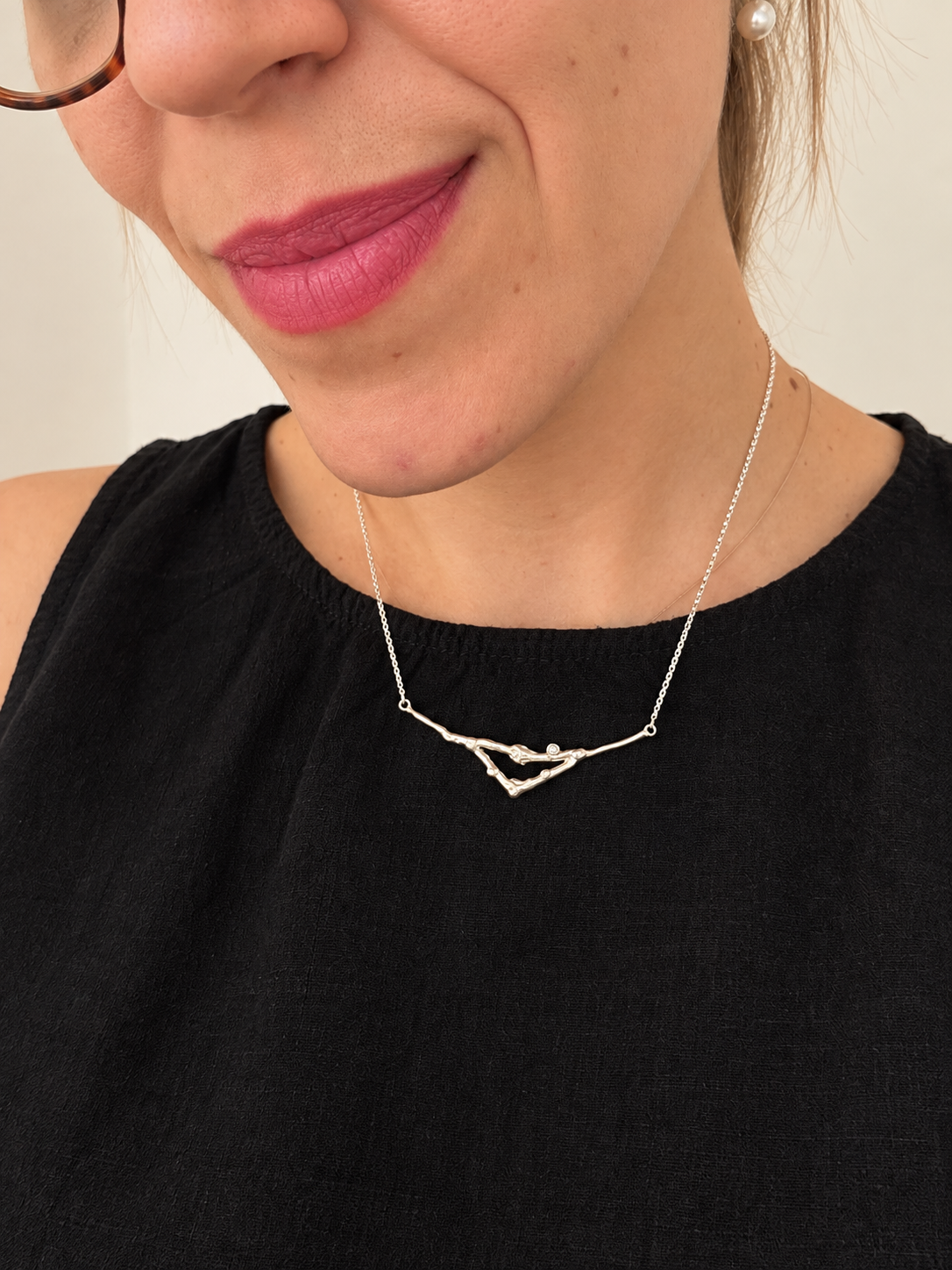 A gold necklace featuring a delicate, organic branch-like pendant with small black bead accents, displayed on a clean white background.