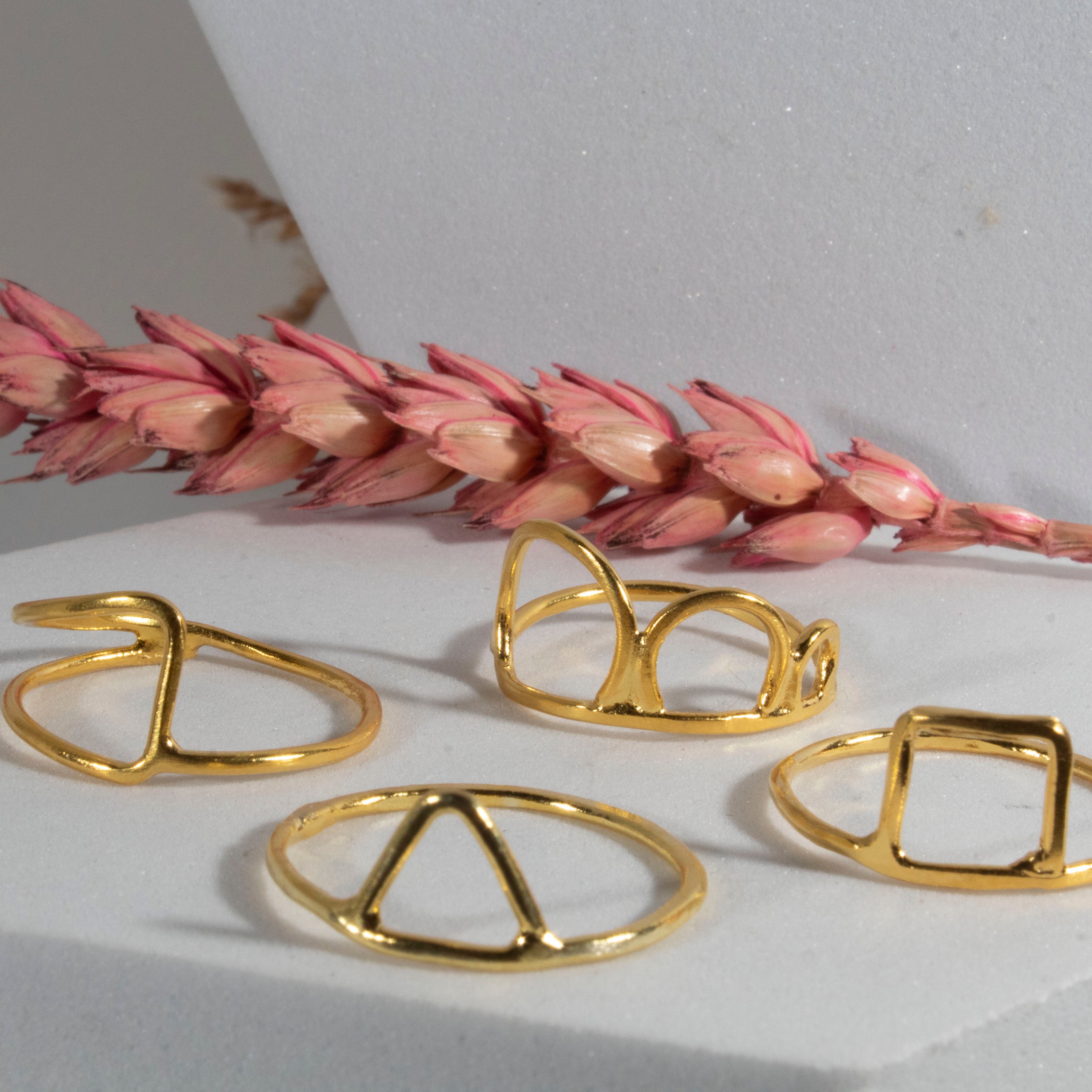 Gold rings on a white surface with pink dried flowers