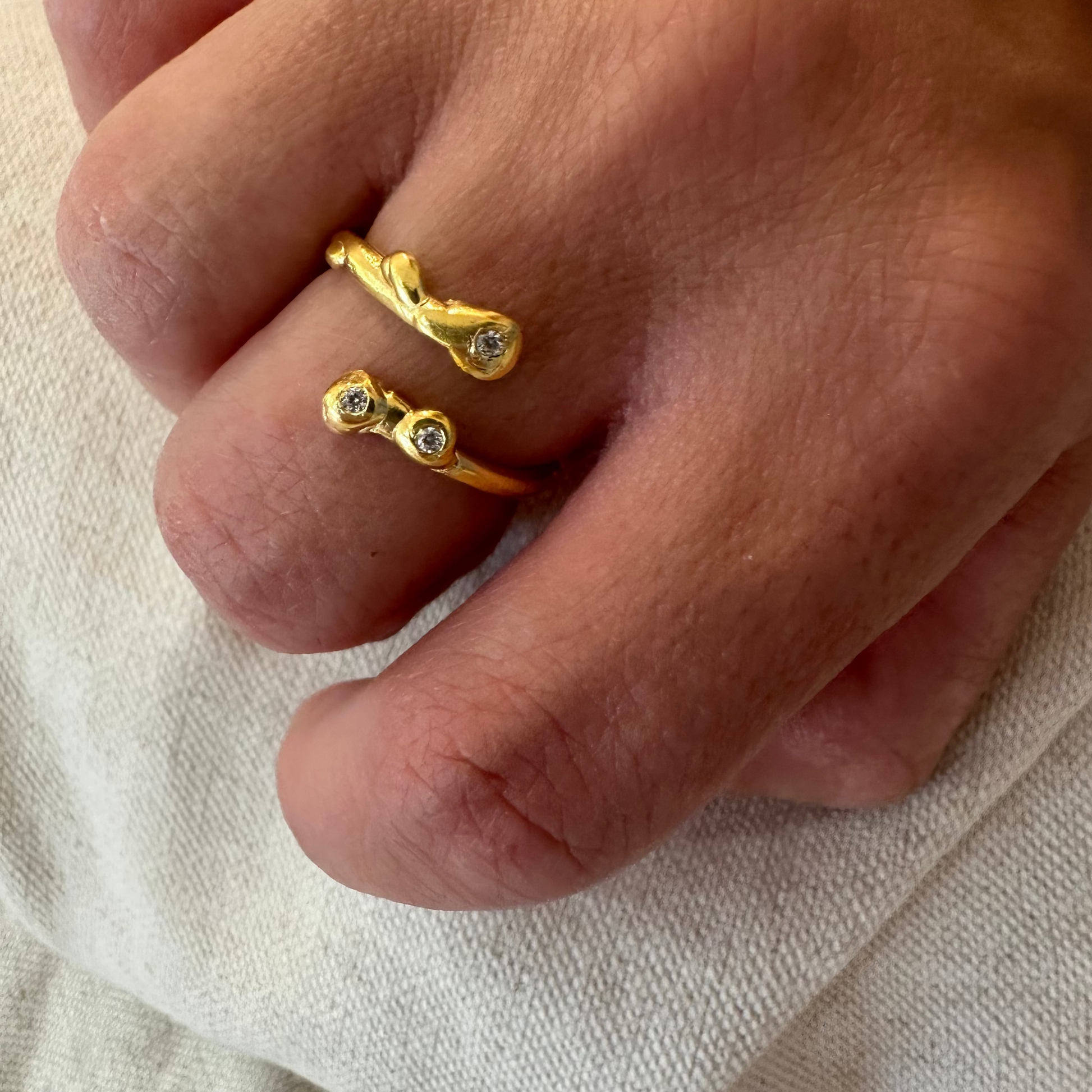 Close-up of a hand wearing two gold rings with small stones on a light fabric background