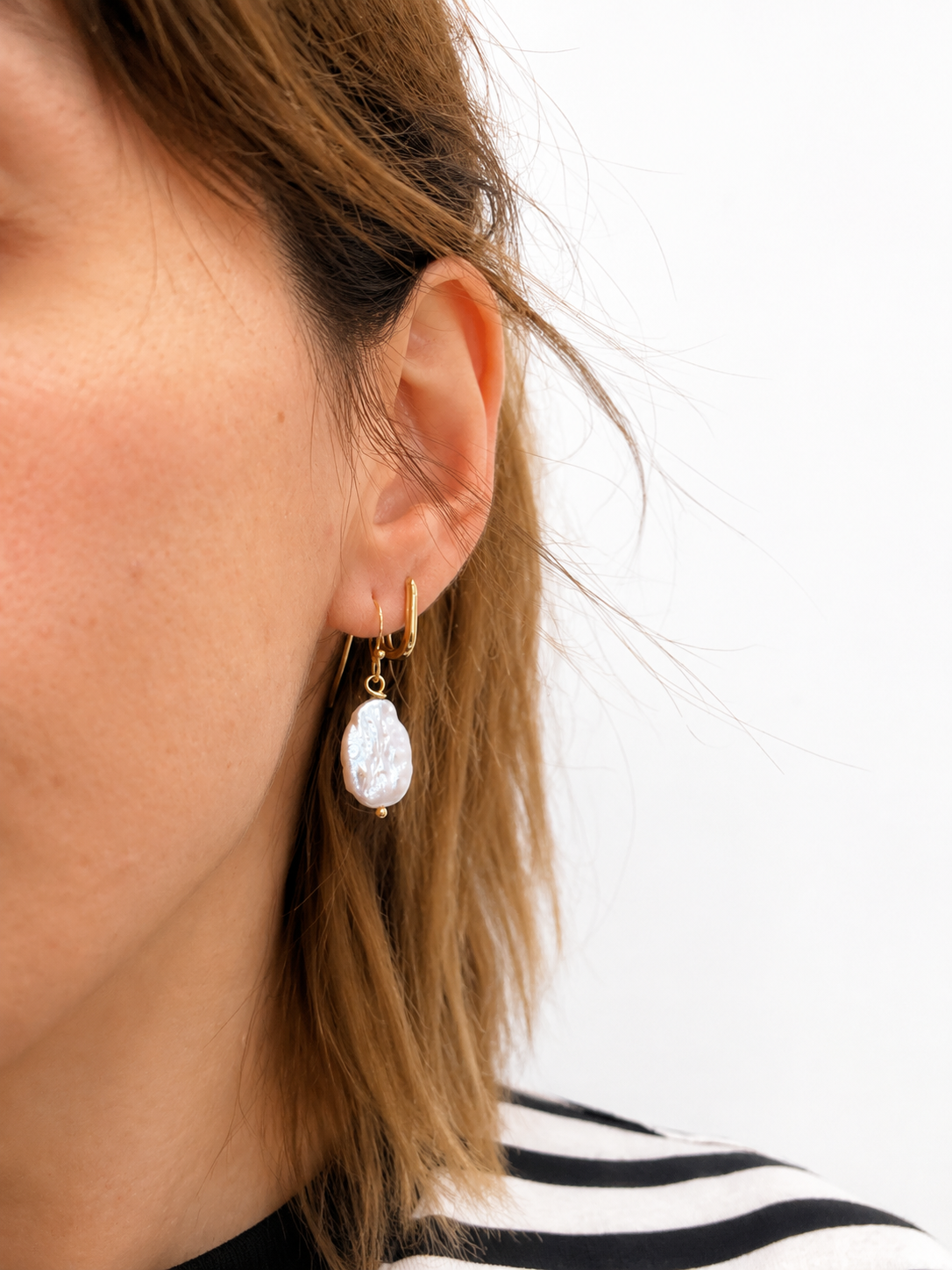 Gold earrings with large, irregularly shaped pearl-like stones on a white background