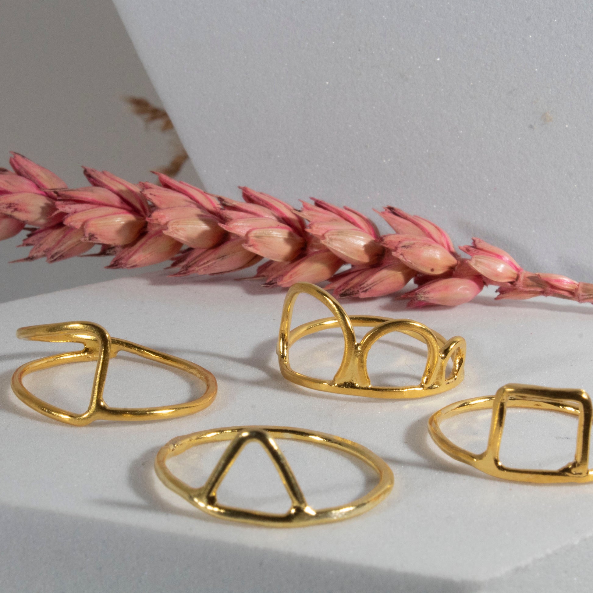 Gold rings on a white surface with pink dried flowers