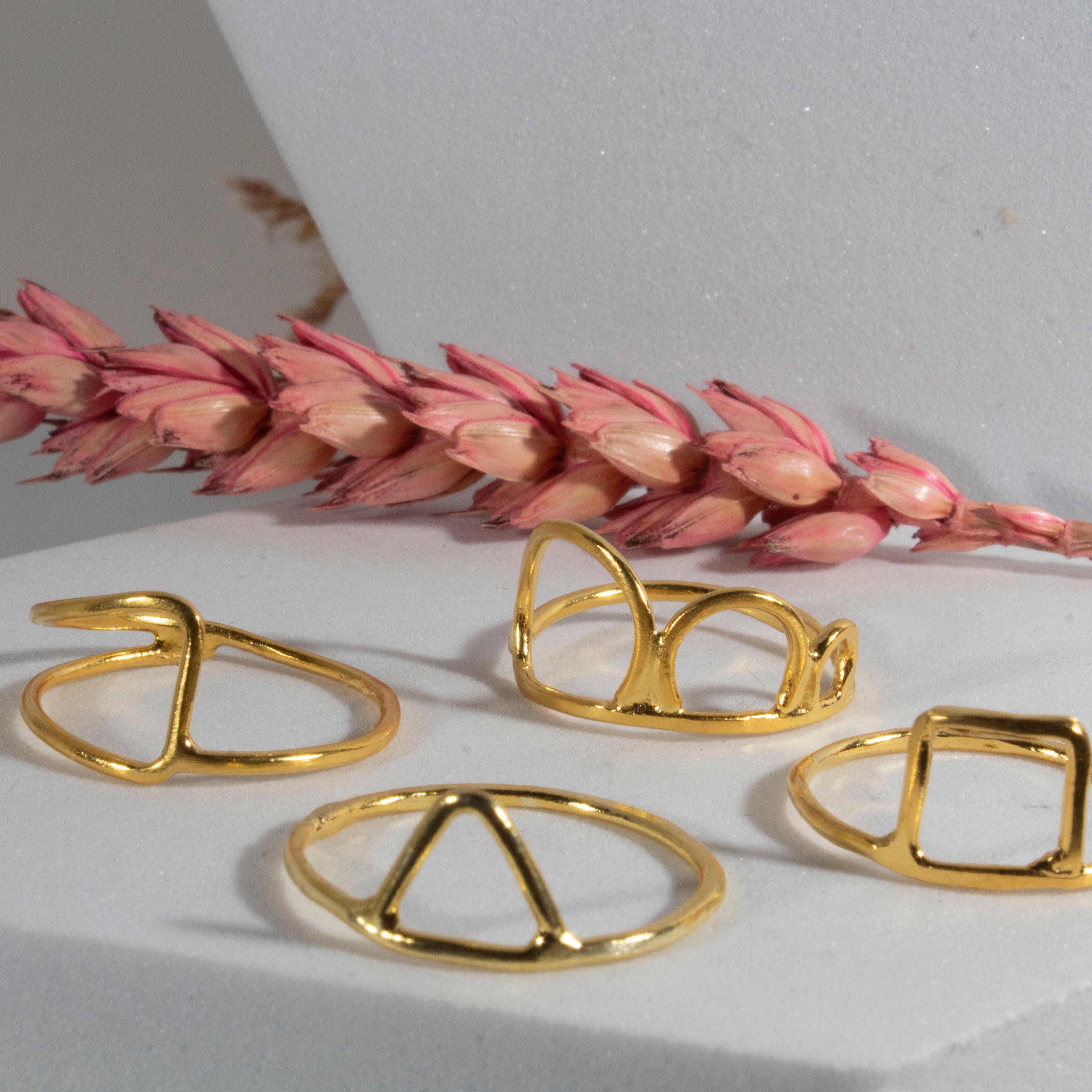 Gold rings on a white surface with pink dried flowers
