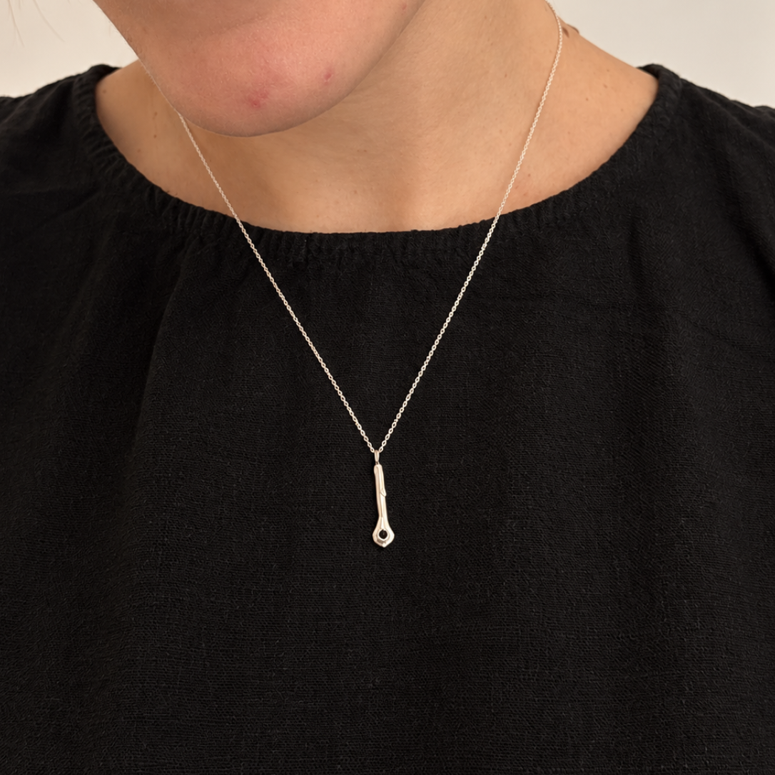 A close-up of a person wearing a delicate silver pendant necklace with a teardrop-shaped drop, styled with a black top against a plain light background.