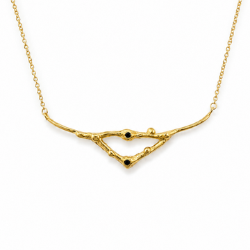 A gold necklace featuring a delicate, organic branch-like pendant with small black bead accents, displayed on a clean white background.