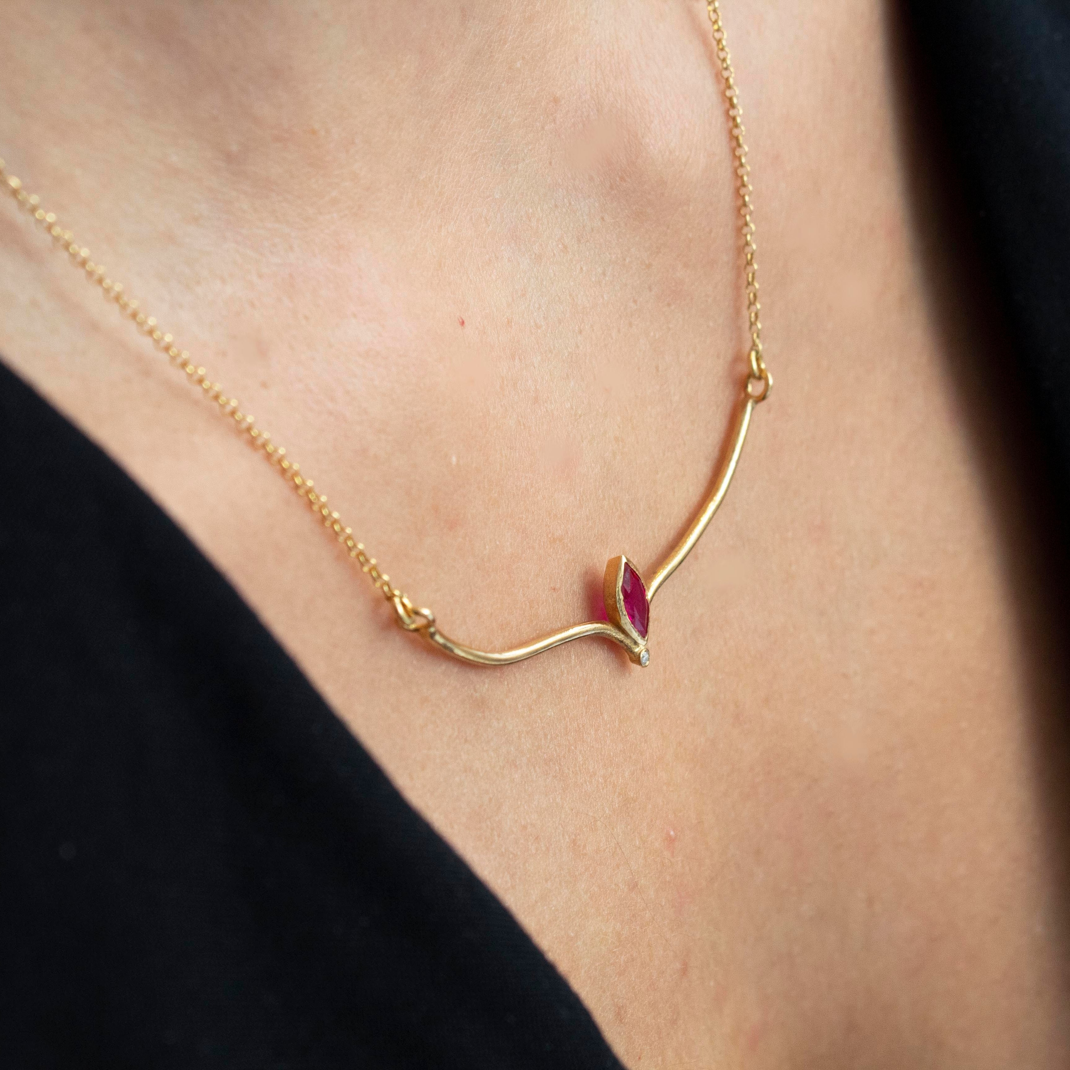 A gold-plated necklace with a red zircon gemstone pendant, displayed on a person's neck.