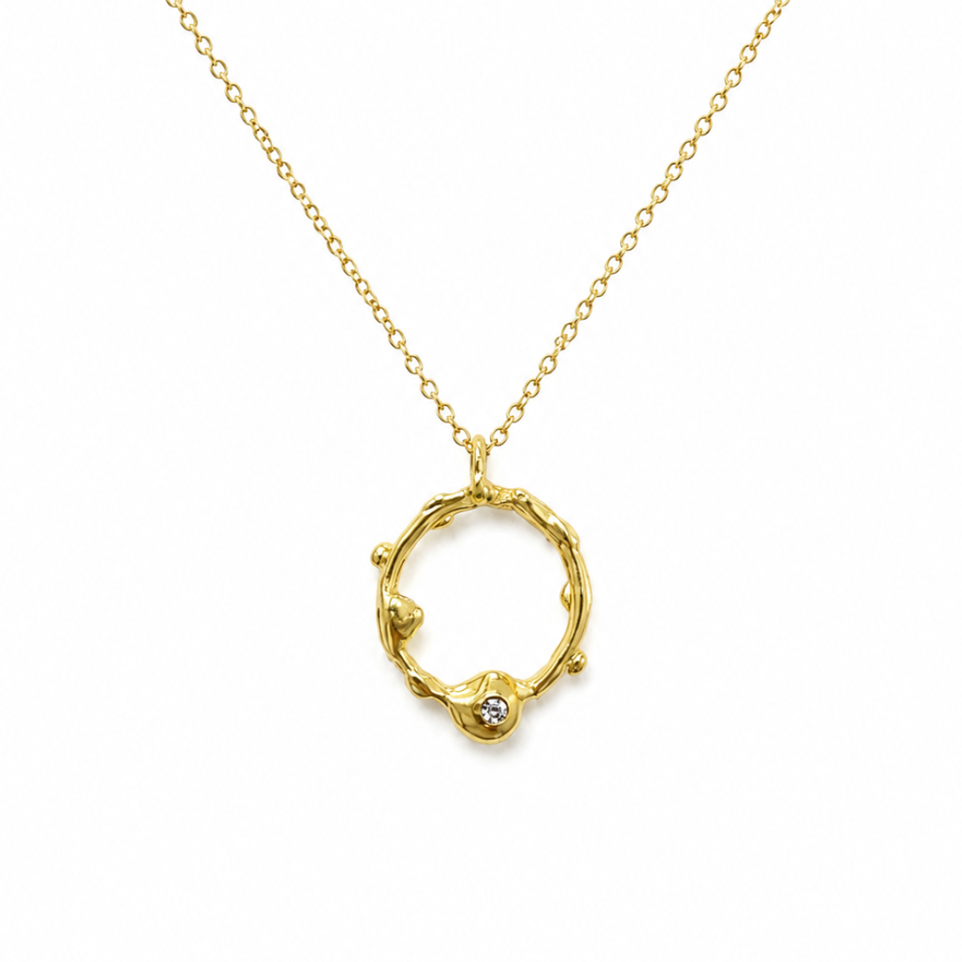 A gold necklace featuring a textured, organic-shaped open ring pendant with a small clear gemstone at the bottom, suspended from a delicate gold chain on a white background.