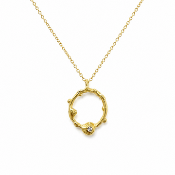 A gold necklace featuring a textured, organic-shaped open ring pendant with a small clear gemstone at the bottom, suspended from a delicate gold chain on a white background.