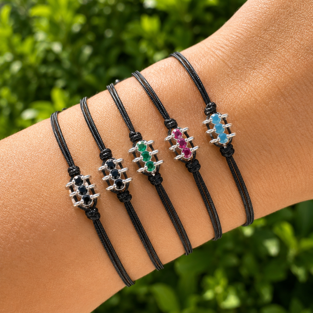 Black cord bracelets with colorful charm elements on a wrist against a green leafy background