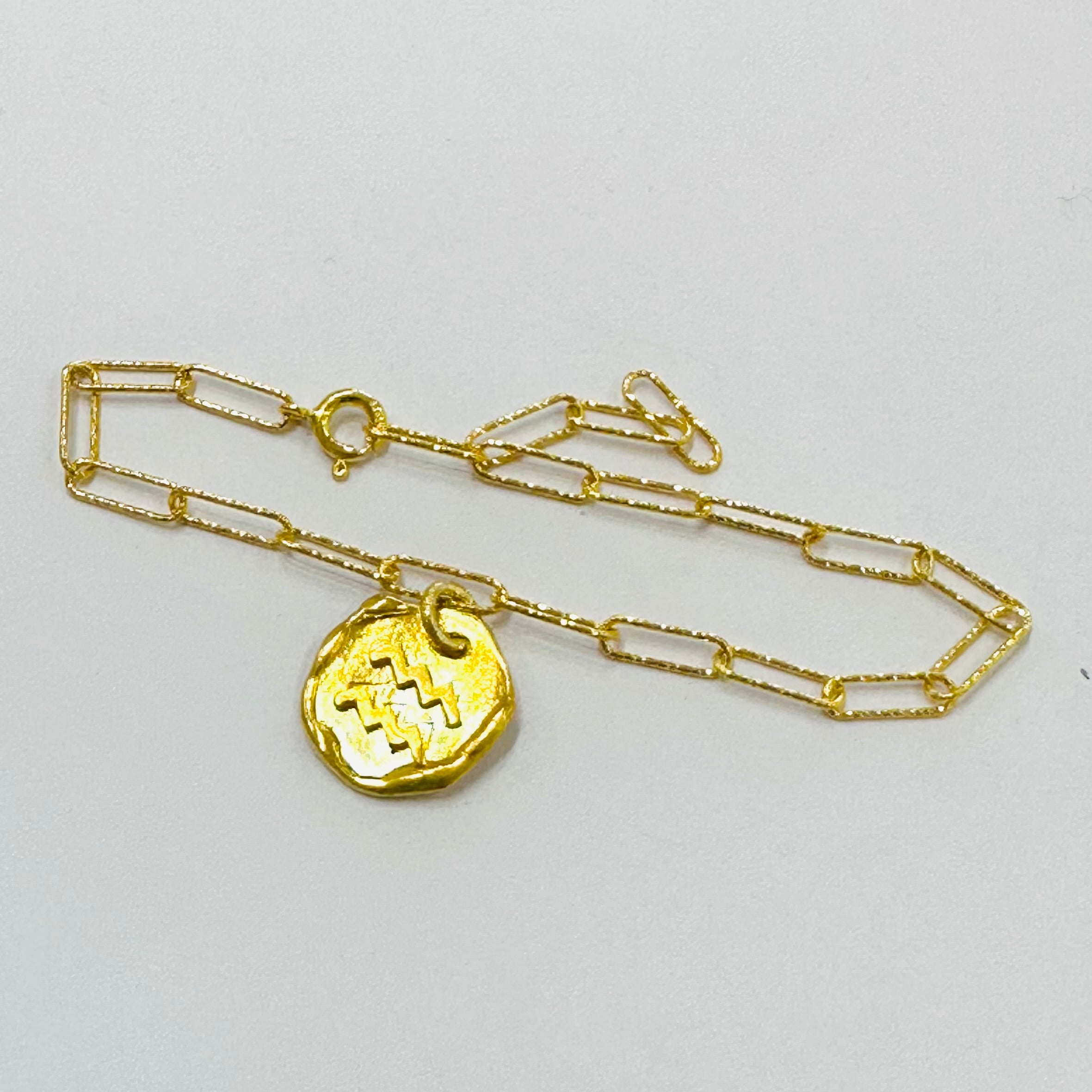 Gold chain necklace with a round pendant on a light gray background